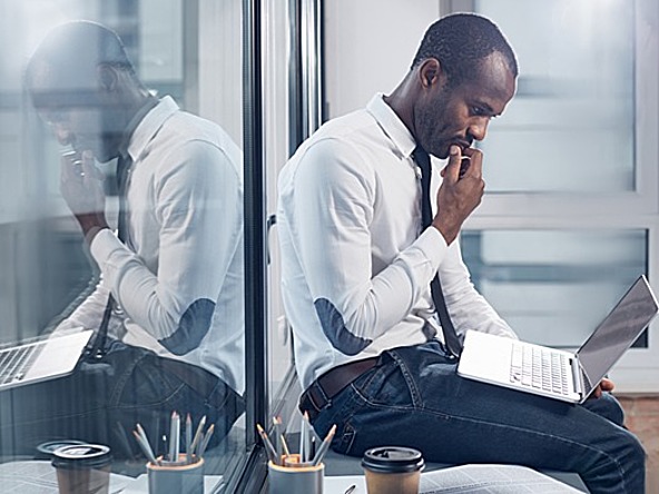 Male executive of colour looks pensively at laptop